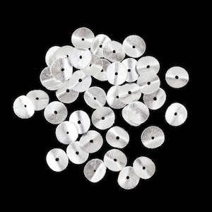 May include: A scattering of silver, circular sequins, each with a central hole, set against a black backdrop. The sequins have a textured, radial design. Suitable for adding detail to garments or craftwork.