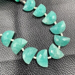 Puede incluir: Un collar o pulsera con cuentas de piedra preciosa de amazonita. Las cuentas son de color verde azulado claro, cortadas en forma de media luna con superficies facetadas. Peque&ntilde;as cuentas blancas unen las piezas de amazonita.