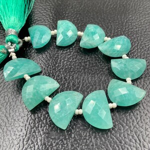 Puede incluir: Un hilo de cuentas de piedras preciosas en forma de media luna azul claro. Cada cuenta est&aacute; facetada y ensartada con peque&ntilde;as cuentas blancas. Una borla verde est&aacute; unida al hilo.