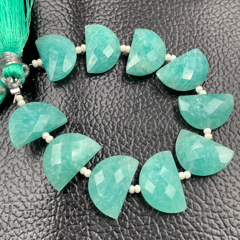 Puede incluir: Un collar de cuentas de piedra preciosa Amazonita. Las cuentas son de color verde azulado claro, cortadas en forma de media luna y facetadas. El collar est&aacute; ensartado con peque&ntilde;as cuentas blancas y una borla verde azulado.