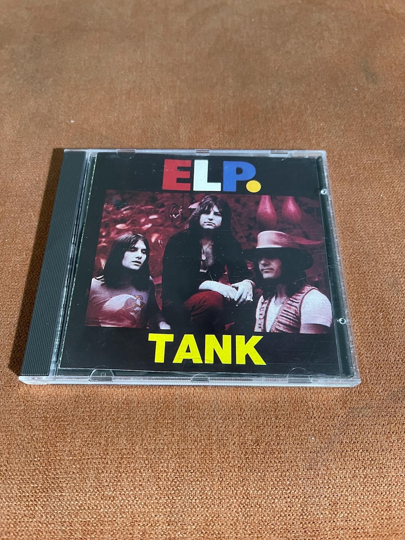 May include: A CD case with a black background and a colourful image of a band called "ELP." The band members are wearing casual clothing and are standing in front of a red and green background. The text "TANK" is printed in yellow letters below the band's name.