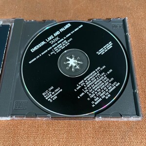 May include: A compact disc (CD) with a black and silver label. The label features the text "Emerson, Lake and Palmer" and "Tank". The CD is a live recording of the band's 1973 world tour. The track list is printed on the label.