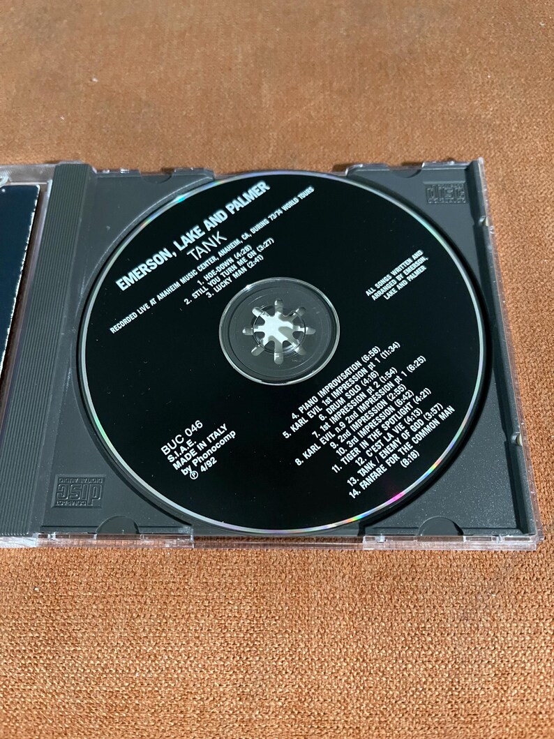 May include: A compact disc (CD) with a black and silver label. The label features the text "Emerson, Lake and Palmer" and "Tank". The CD is a live recording of the band's 1973 world tour. The track list is printed on the label.
