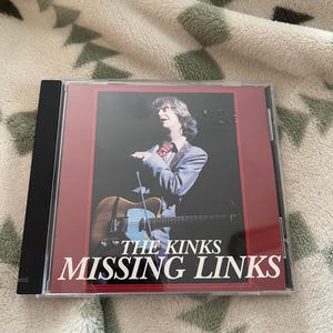 May include: A CD case featuring the album "Missing Links" by The Kinks. The cover art shows a man with long hair holding a guitar. The album title and band name are in white text against a dark red background.