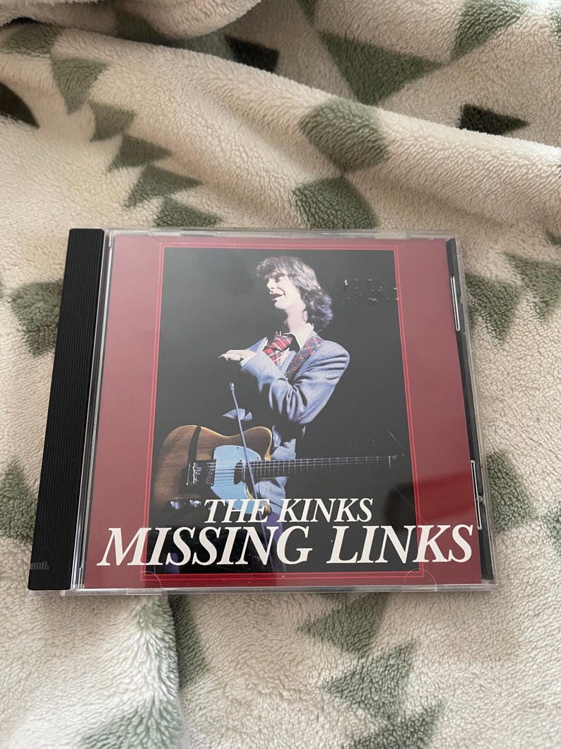 May include: A CD case featuring the album "Missing Links" by The Kinks. The cover art shows a man with long hair holding a guitar. The album title and band name are in white text against a dark red background.