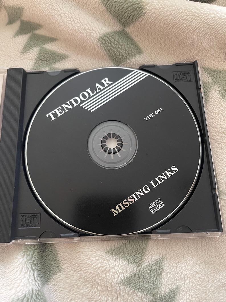 May include: A black compact disc with the text "TENDOLAR" and "MISSING LINKS" in white. The disc is in a clear plastic case. The disc also has the text "TDR-081".