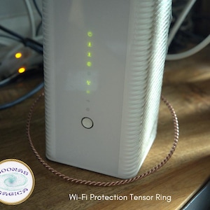 May include: A white Wi-Fi router with a copper wire ring around it. The router has a series of green lights on the front. The text "Wi-Fi Protection Tensor Ring" is printed below the router.