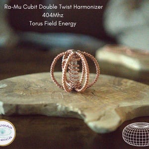 以下が含まれることがあります： Ra-Mu Cubit Double Twist Harmonizer 404Mhz Torus Field Energy。中央に透明なクリスタルのロッドがあり、それをねじれた銅線の球状ケージが囲んでいます。画像にはテキストラベルとトーラスのワイヤーフレームグラフィックが含まれています。