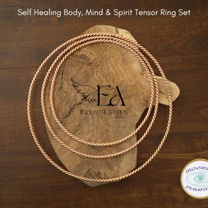 May include: Set of three copper wire tensor rings, each with a braided design. The rings are stacked on top of each other on a wooden surface. The text "Self Healing Body, Mind & Spirit Tensor Ring Set" is at the top of the image. The text "EA Frequencies" is in the center of the image.
