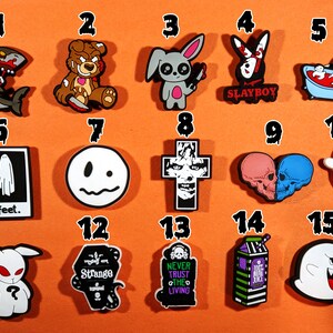 May include: A selection of fifteen brightly coloured shoe charms featuring gothic and spooky designs. The charms include a zombie shark, a teddy bear with a knife, a bunny with a knife, a bunny with the text "SLAYBOY", a skeleton in a bathtub, ghosts, skulls, and other Halloween-themed images.