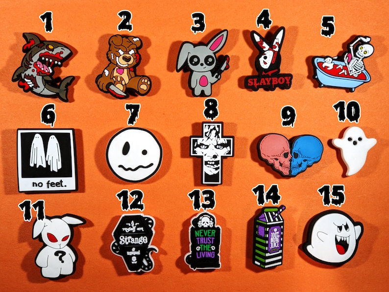 May include: A selection of fifteen brightly coloured shoe charms featuring gothic and spooky designs. The charms include a zombie shark, a teddy bear with a knife, a bunny with a knife, a bunny with the text "SLAYBOY", a skeleton in a bathtub, ghosts, skulls, and other Halloween-themed images.