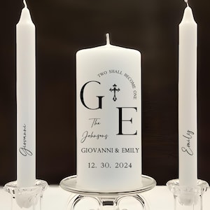 May include: Two white unity candles with the text "Two shall become one" and "G+E The Johnsons GIOVANNI & EMILY 12. 30. 2024" on the larger candle.