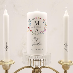 Peut inclure: Deux bougies d'unité blanches avec les noms Megan et Austin écrits dessus, et une bougie blanche plus grande avec un motif de couronne florale et les initiales M et A, les noms Megan et Austin, et la date 07.19.2026.