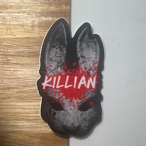 May include: A black and white sticker of a rabbit mask with red blood splatters and the word "KILLIAN" written in red across the forehead.