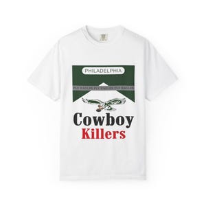 Könnte beinhalten: Ein weißes Kurzarm-T-Shirt mit einem Grafikdesign, das einer Zigarettenschachtel nachempfunden ist. Das Design enthält den Text PHILADELPHIA, FLY EAGLES, Cowboy und Killers sowie eine Abbildung eines Adlers mit einem Football.