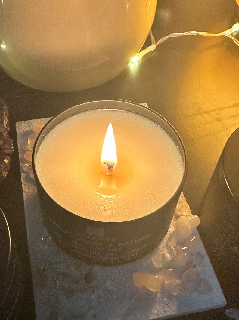 May include: A black candle jar with a white soy wax candle burning inside. The candle is labelled "Handcrafted Natural Soy Wax Candle" and "Made with Love".