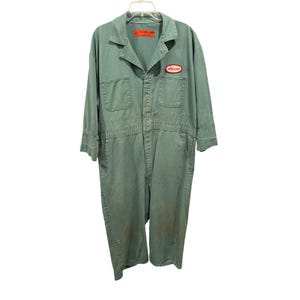 May include: A sage green utility jumpsuit featuring a collared neckline, long sleeves, and a button-up front. The garment includes two chest pockets, an oval patch with the name Allison in red text, and an orange interior neck label.
