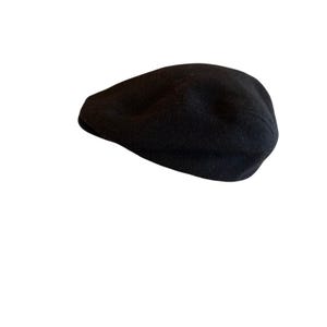 May include: A solid black beret crafted from a soft, felted material. The hat features a rounded, flat-topped crown with a structured edge, maintaining a smooth, uniform texture across the entire surface of the headwear accessory.