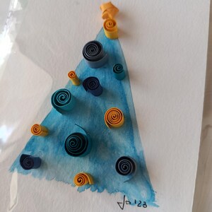 Pode incluir: Ilustração de uma árvore de Natal em aquarela com enfeites de quilling de papel azul e amarelo. A árvore é pintada em tons de azul, encimada por uma estrela. Assinado "Ja'23".