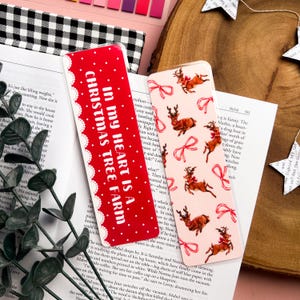 May include: Two Christmas-themed bookmarks. The first bookmark is red with white text that reads "In my heart is a Christmas Tree Farm". The second bookmark is pink with a repeating pattern of white reindeer and red bows.