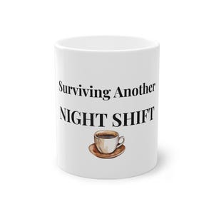 Puede incluir: Taza de café de cerámica blanca con el texto "Surviving Another NIGHT SHIFT" en negro. Una ilustración de acuarela de una taza de café y un platillo está debajo del texto. La taza es de tamaño estándar.