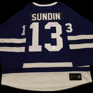 May include: A blue hockey jersey with white stripes and the number 13 on the back. The name "SUNDIN" is above the number. The jersey is signed by the player.