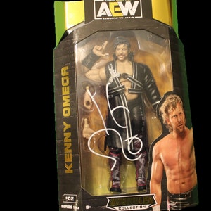 May include: A black and gold action figure of Kenny Omega in a black robe with a white and pink design. The figure is in a plastic display case with a black and gold background. The figure is part of the AEW Unrivaled Collection.