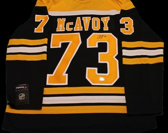 May include: Black and gold hockey jersey with the number 73 and the name McAvoy on the back. The jersey has white stripes on the sleeves and bottom.