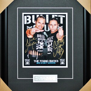May include: Framed print featuring The Young Bucks, Nick & Matt Jackson, in black and white. The print includes signatures and the text "BULLET CLUB". The frame is black with a white mat.