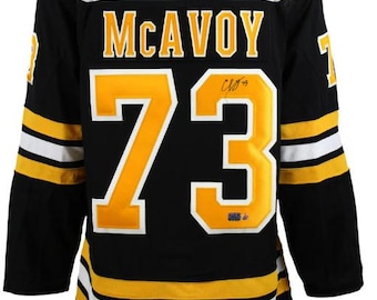 May include: Black hockey jersey with yellow and white stripes. The back of the jersey has the name "MCAVOY" and the number "73" in yellow. The jersey is signed in black.