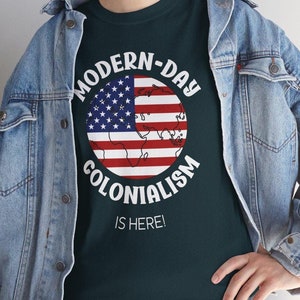 May include: A dark green t-shirt with a white circle graphic that says "MODERN-DAY COLONIALISM IS HERE!" The graphic features a globe with the American flag design.