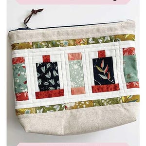May include: A rectangular, beige fabric pouch with a zipper closure and a brown leather pull. The front features a patchwork design with three rectangular panels, each with a different patterned fabric. The text "Spools on Parade Pouch" is at the top.