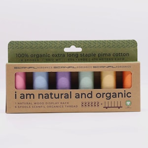 May include: A rectangular cardboard box containing six spools of Scanfil Organics extra long staple pima cotton thread in pink, light blue, purple, mint green, yellow, and orange. The box text reads 100% organic extra long staple pima cotton.