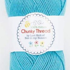 May include: A ball of turquoise chunky thread, wrapped with a white label. The label features the text "Chunky Thread" in red, with the words "100% Cotton" and "by Lori Holt of Bee in my Bonnet". The thread is tightly wound and ready for crafting.