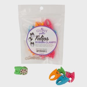 May include: A clear plastic bag contains colorful bobbin clamps. The clamps are in shades of pink, orange, blue, and green. The bag has a label that reads "Tulips BOBBIN CLAMPS" and includes the text "the GYPSY quilter".