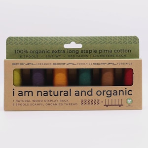 May include: A rectangular cardboard box containing six spools of Scanfil Organics thread in lime, purple, orange, green, brown, and red. The box features the text 100% organic extra long staple pima cotton, 6 spools, 50/2 wt, 500 yards, and i am natural and organic.