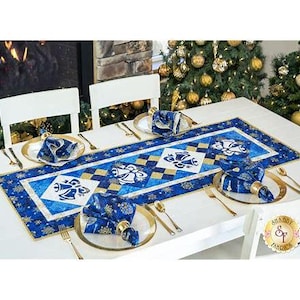 May include: A blue and gold table runner with a snowflake and bell design. The runner is set on a white table with four place settings. Each place setting includes a blue and gold napkin, a gold fork, and a gold knife.