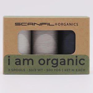 May include: A rectangular cardboard box labeled SCANFIL ORGANICS and i am organic containing three spools of thread in white, light gray, and black. The packaging text specifies 3 spools, 50/2 wt, 500 yds, and 457 m each for the thread contents.