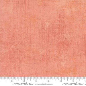 May include: A textured fabric with a peach-colored background and subtle vertical and horizontal brushstroke effects. The fabric has a mottled appearance with variations in color and texture. A ruler with inch measurements is at the bottom.