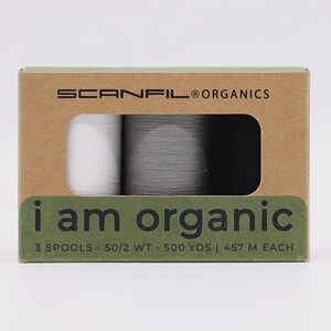 May include: A rectangular cardboard box containing three spools of thread in white, gray, and black. The packaging is labeled SCANFIL ORGANICS and i am organic, with text indicating 3 spools, 50/2 WT, and 500 YDS or 457 M of thread per spool.