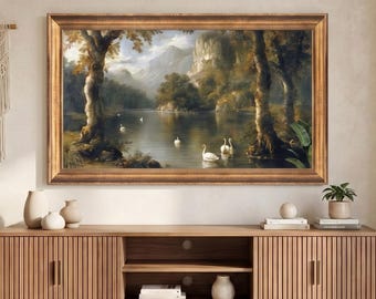 Op de afbeelding: Een rechthoekig landschapsschilderij in een gouden lijst met een meer met witte zwanen, bomen en bergen, gemonteerd boven een lang, houten tv-meubel met latten, twee kasten en een open middenplank met boeken en een witte vaas.