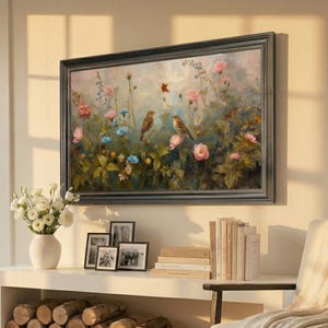 Pode incluir: Uma pintura emoldurada de flores e pássaros está pendurada acima de uma prateleira branca. A prateleira contém livros, fotos emolduradas e um vaso de flores brancas. Uma pilha de lenha está embaixo, e um cobertor creme está em uma cadeira.