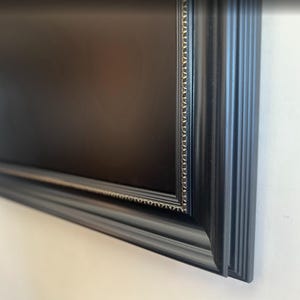 May include: A rectangular picture frame with a matte black finish and a decorative inner border featuring a repeating gold-toned pattern. The frame has a multi-layered, stepped profile that creates depth and dimension along the outer edges.
