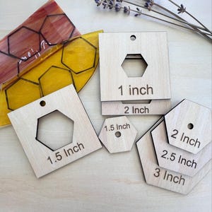 Può includere: Modelli esagonali in legno di varie dimensioni, da 2,5 cm a 7,6 cm. Ogni modello ha un ritaglio esagonale ed è etichettato con la sua dimensione in pollici. Ci sono anche due pezzi di vetro colorato con un motivo esagonale.