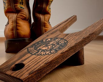 May include: A wooden boot jack with the text "FAT DOG BOOT JACKS" and a circular emblem. The boot jack is made of dark wood and has a slot for pulling off boots. Brown leather cowboy boots are in the background.