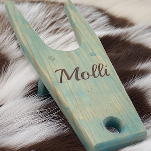 May include: A light blue wooden boot jack with a hole in the bottom and the name "Molli" engraved on the side.