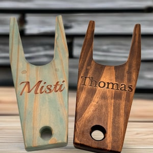 May include: Two wooden boot jacks, one is light blue with the name "Misti" engraved on it, the other is dark brown with the name "Thomas" engraved on it.