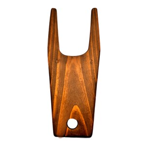 May include: A wooden boot jack with a dark brown stain. The jack has a rounded top with two prongs and a hole in the center.