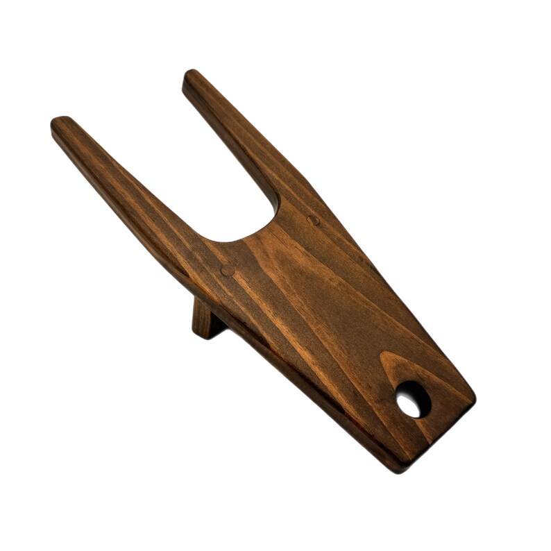 May include: A wooden boot jack with a dark brown stain. The jack has a U-shaped opening and a rounded bottom.