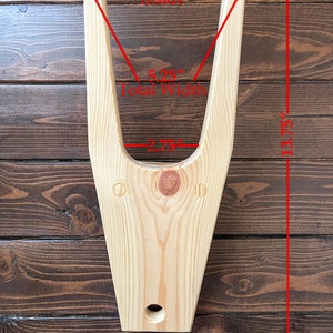 May include: Wooden V-shaped stand with a 4-inch inside width, 5.25-inch total width, and 13.75-inch height. The stand is made of light wood and has a hole in the bottom.